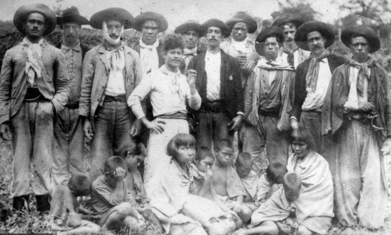 Em pé, 'bugreiros' posam com indígenas do povo Xokleng capturadas, em foto feita provavelmente nos anos 60